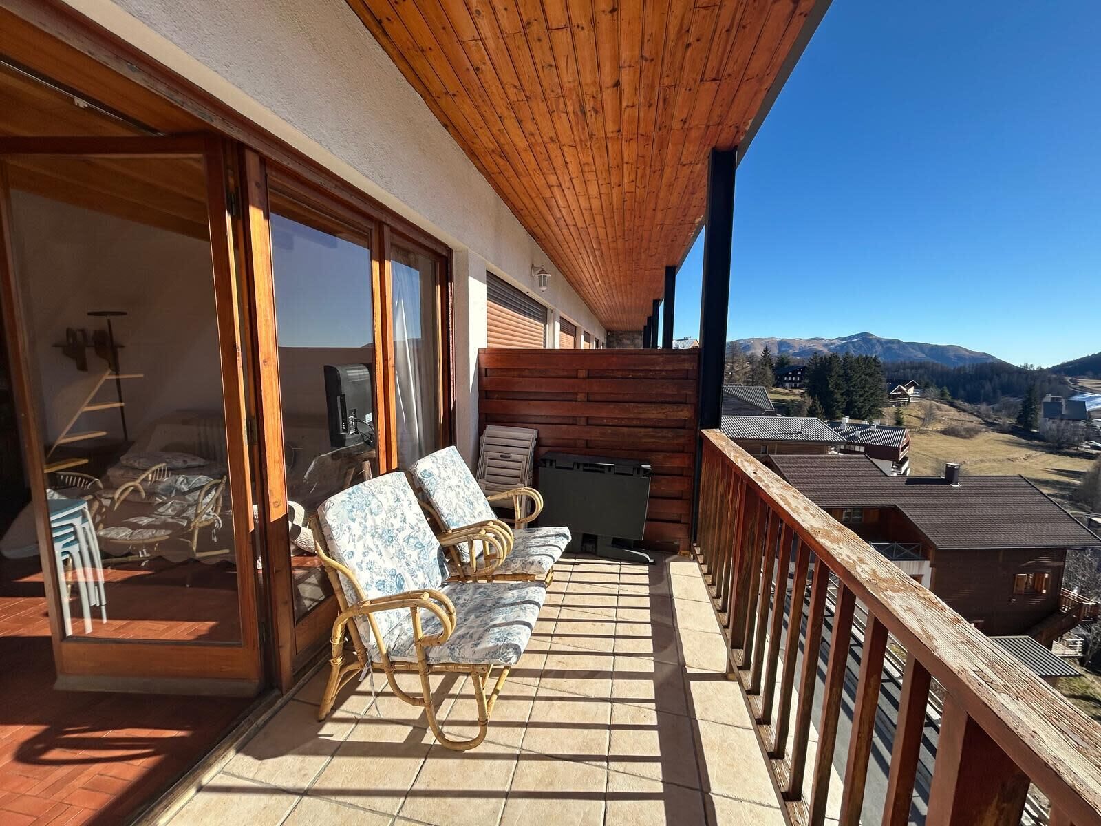 A balcony with wicker chairs and a table, overlooking a mountainous landscape.