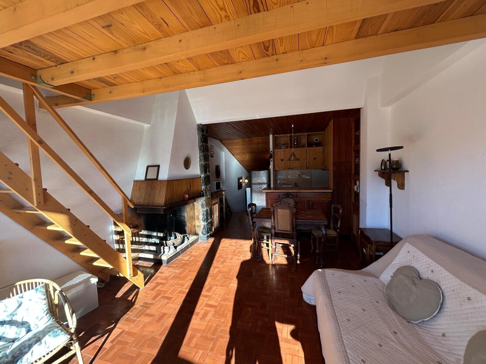 Ein gemütlicher Innenraum mit einer Holztreppe, einem Kamin, einer Küchenzeile und einem Wohnbereich mit einer Couch.