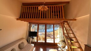Une pièce de style loft avec un plafond en bois, un téléviseur posé sur un meuble, un canapé et une vue sur un paysage enneigé à travers de grandes portes vitrées.