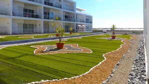 A modern hotel with multiple balconies, a well-maintained lawn with geometric patterns, and a clear view of the sea. - Fuseta Formosa Village (Olhao)