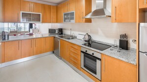A modern kitchen with wooden cabinets, stainless steel appliances, a microwave, a coffee maker, and a dishwasher. - Fuseta Formosa Village (Olhao)