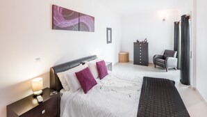 A bedroom with a bed, nightstand, dresser, chair, and artwork on the wall. - Fuseta Formosa Village (Olhao)