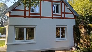 Una casa de dos pisos con techo a dos aguas, paredes exteriores blancas y estructura de madera en rojo.