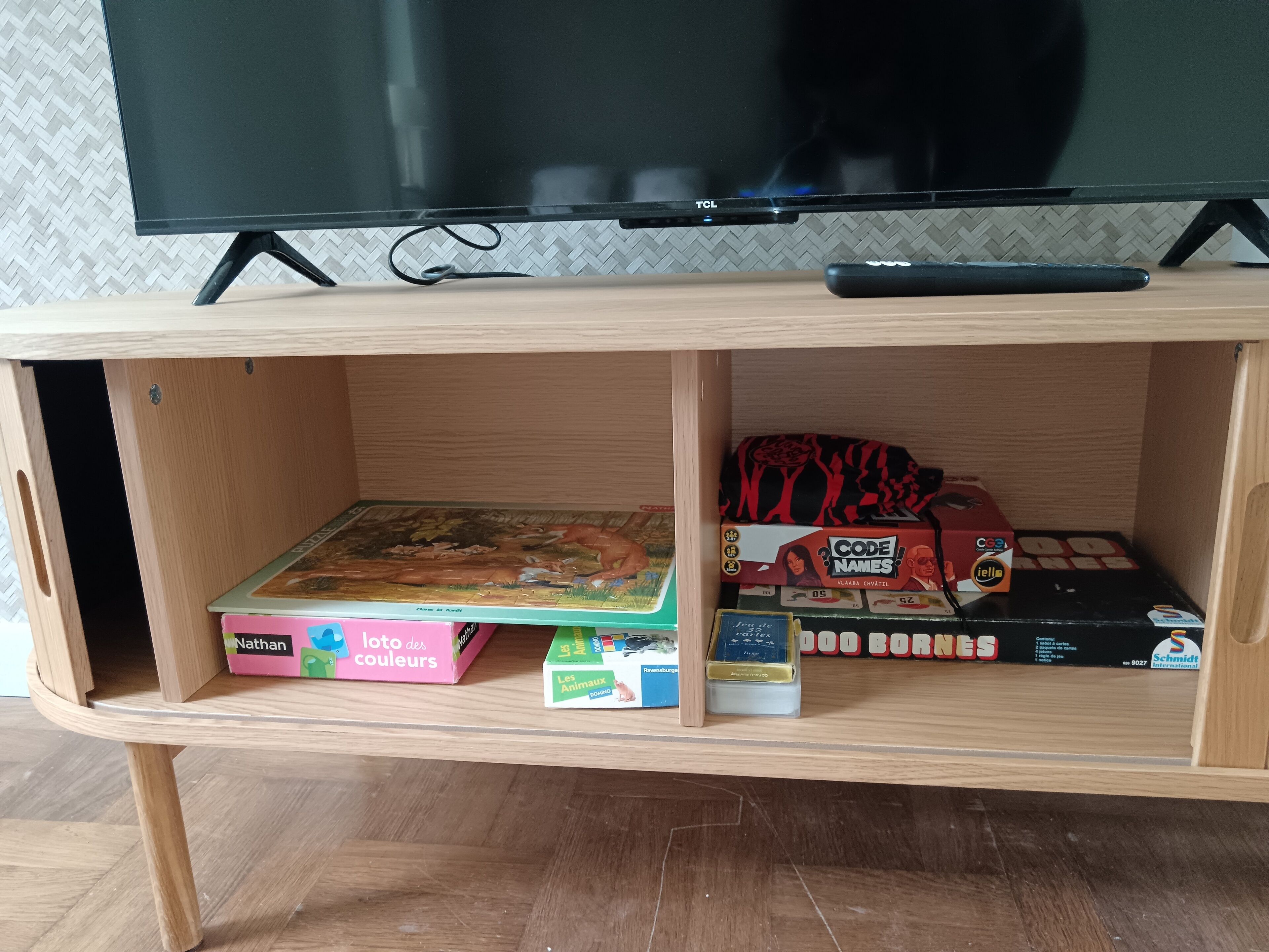 Un'unità di intrattenimento in legno con una TV a schermo piatto, un telecomando e diversi giochi e libri per bambini.