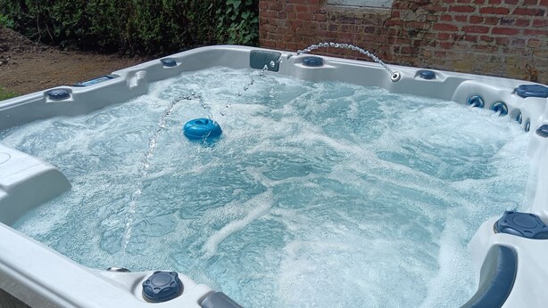 Un jacuzzi con un aro inflable azul, rodeado por una terraza de madera y un muro de ladrillo.