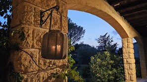 A stone archway with a hanging lantern, surrounded by greenery and trees. - Cozy vacation home with a heated pool, hot tub, and sauna. Pets allowed. (Castillon-du-Gard)