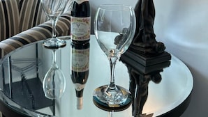 Une table ronde en verre, avec une bouteille de vin, deux verres à vin et une lampe décorative.