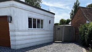 Une allée de gravier mène à un bâtiment blanc doté d’une porte et de fenêtres en bois.