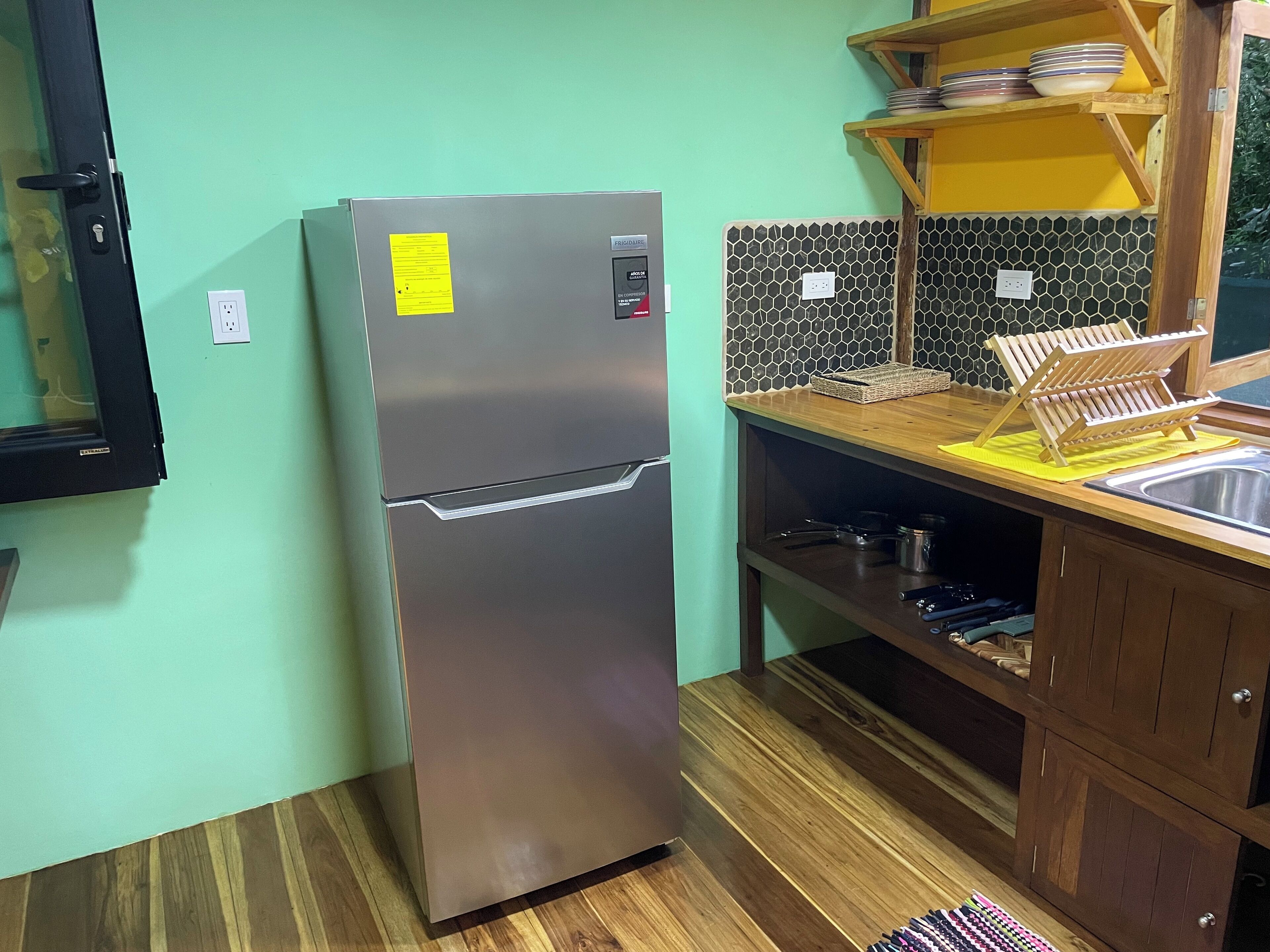 A kitchen with a stainless steel refrigerator, wooden cabinets, a tiled backsplash, and a wooden countertop with a dish rack.