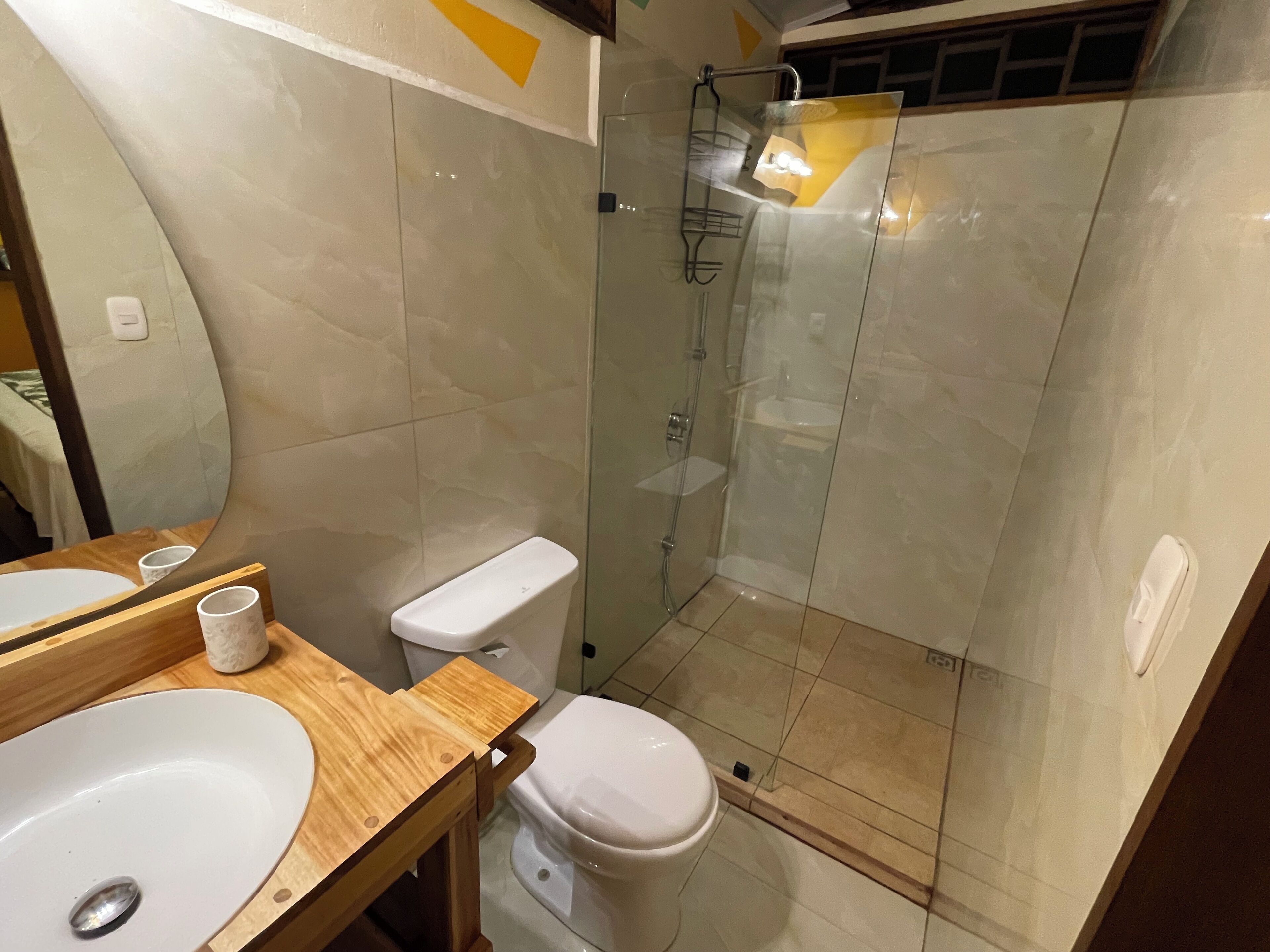 A bathroom with a wooden vanity, a white sink, a toilet, and a glass-enclosed shower area.