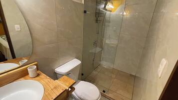 A bathroom with a wooden vanity, a white sink, a toilet, and a glass-enclosed shower area.