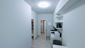 En smal hall med trägolv, vita väggar och en taklampa. I slutet av hallen finns en dörr som leder in till ett annat rum.