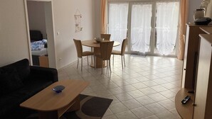 Un salon comprenant un canapé, une table basse, une table à manger avec des chaises, ainsi qu’un coin cuisine avec des placards et un réfrigérateur.