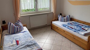 Une pièce avec deux lits en bois, une fenêtre avec des rideaux, un radiateur et une décoration murale représentant un voilier.