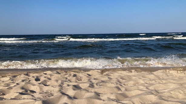 Une plage de sable où les vagues viennent se briser sur le rivage, sous un ciel dégagé.