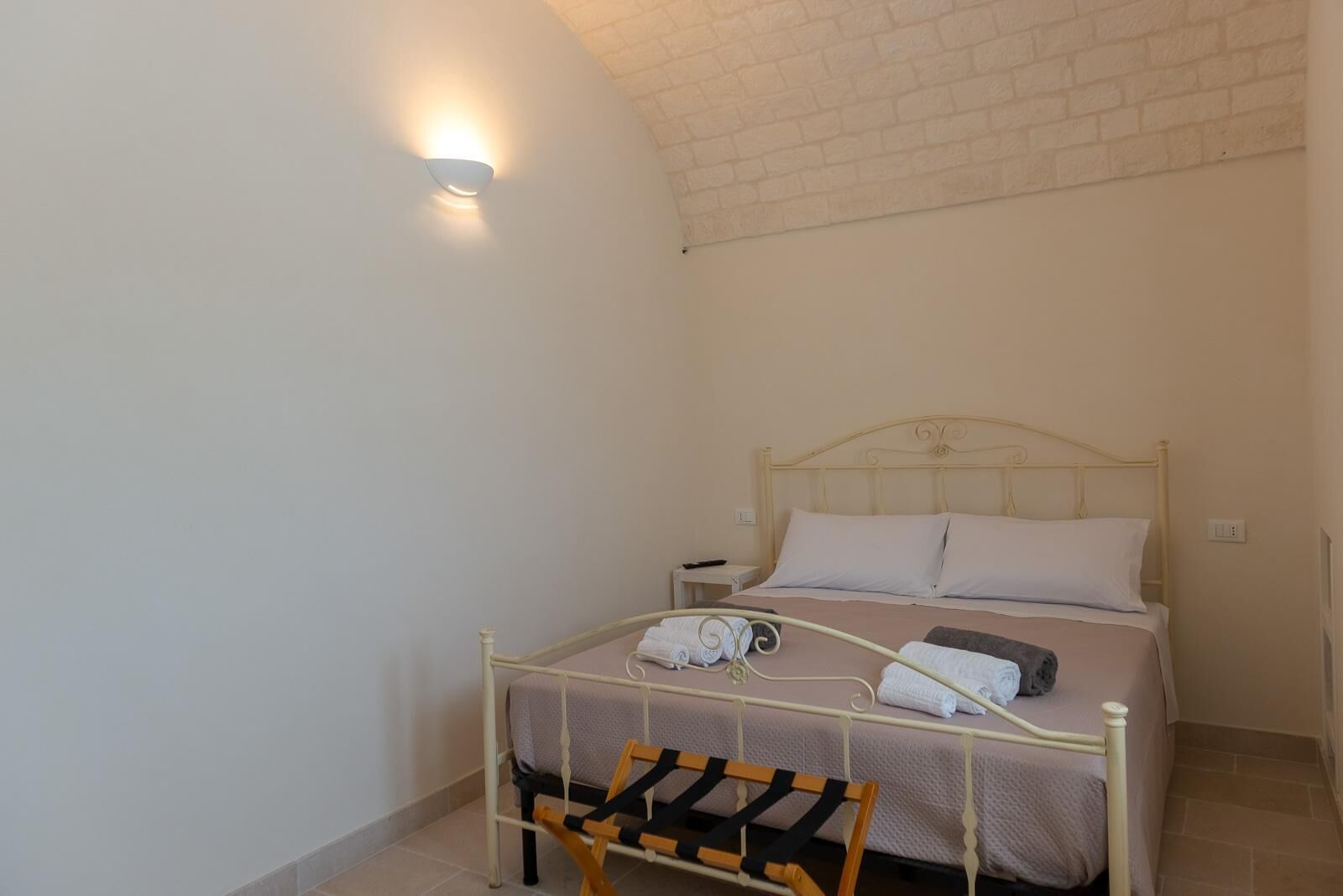 A single bed with a headboard, a bedside table, and a wall-mounted light fixture.