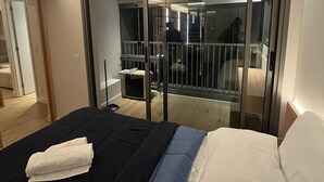 Un dormitorio con cama, puerta corrediza de vidrio que da a un balcón y un baño a la vista.