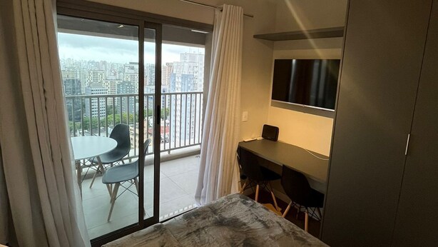 Habitación de hotel con cama, escritorio, silla, televisión y balcón con vista a la ciudad.