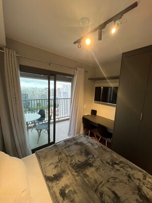 Een hotelkamer met een bed, bureau, stoel, televisie en balkon met uitzicht op de stad.