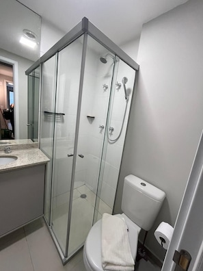 Un baño moderno con ducha de vidrio, inodoro y lavabo con espejo.