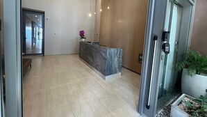 Una moderna zona de recepción con un mostrador de mármol, un panel de pared de madera y una puerta de ascensor de vidrio.
