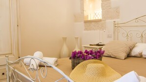 Une chambre à coucher avec un lit, une table de chevet, une lampe, un fauteuil en osier et un panier de fleurs.