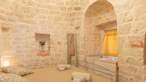A stone-walled room with a bed, pillows, a mirror, and a window with curtains. - Trullo Sorgente - Ostuni (Ostuni)