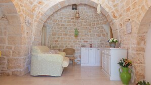 A cozy room with a stone wall, a sofa, a wicker chair, a cabinet, and a green vase with flowers. - Trullo Sorgente - Ostuni (Ostuni)