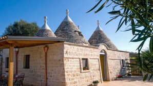 A stone building with three conical roofs, a wooden pergola, and a small table with chairs. - Trullo Sorgente - Ostuni (Ostuni)