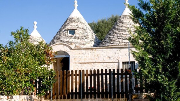 A stone building with three conical roofs and a wooden fence in front. - Trullo Sorgente - Ostuni (Ostuni)