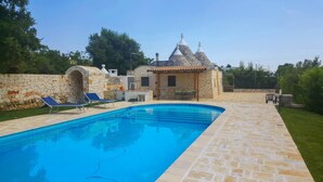 A swimming pool with stone tiles, a stone wall, and a small building with a tiled roof. - Trullo Sorgente - Ostuni (Ostuni)