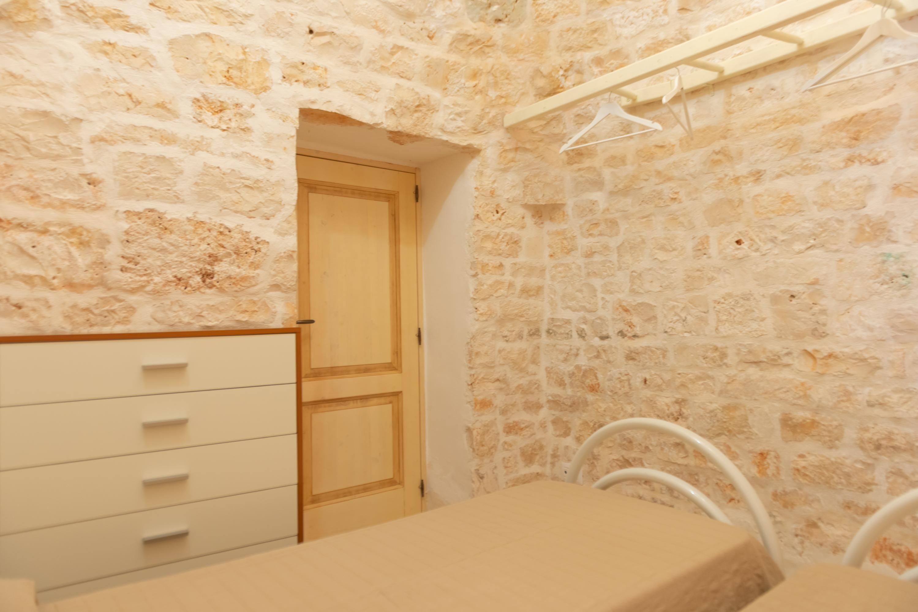 Ein Zimmer mit Steinwand, Holztür, weißem Schminktisch und einem Metallstuhl.