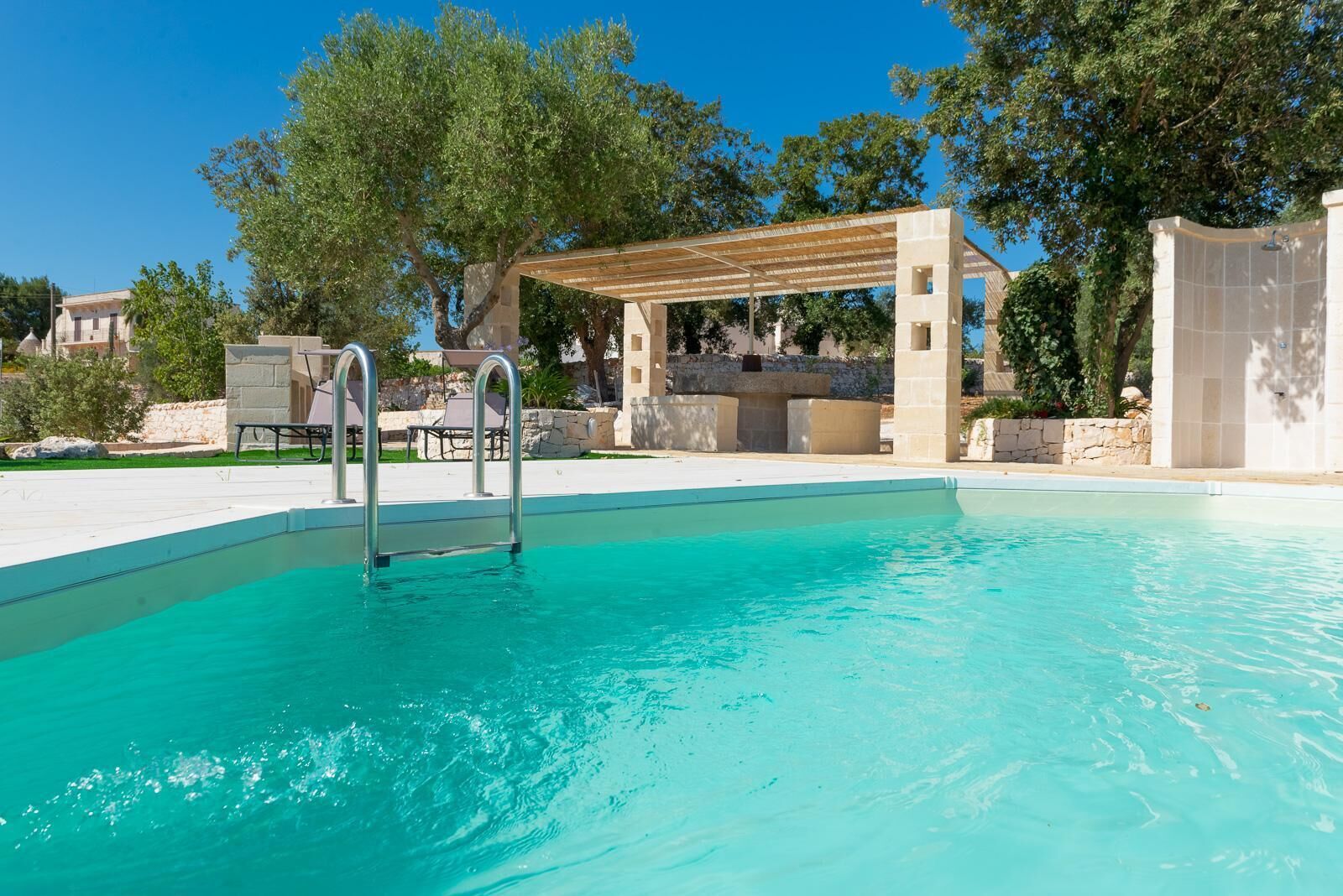 A swimming pool with clear blue water, a pergola, and a stone wall.