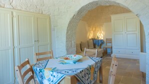 A dining area with a table set for two, a stone archway, and a cozy seating area with a lamp. - Trulli Dei Ciclamini - Locorotondo (Locorotondo)