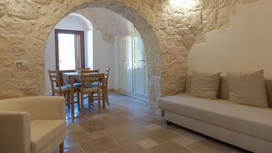 A room with a stone wall, a dining area with a table and chairs, and a sofa. - Trulli Dei Ciclamini - Locorotondo (Locorotondo)