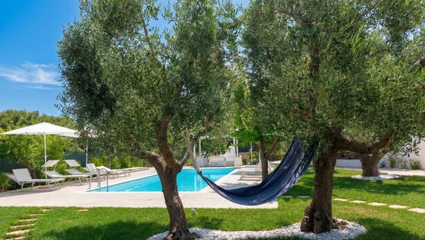 A pool area with a hammock between two trees, surrounded by white pebbles and a grassy lawn.