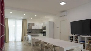 A modern kitchen with white cabinets, a central island with stools, a built-in oven, and a large flat-screen TV on a white stand.