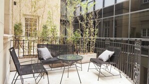 Un balcón con mobiliario exterior, incluyendo una mesa y dos sillas, rodeado de plantas de bambú.