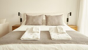 Una cama bien tendida con dos almohadas, una mesita de noche con una lámpara y dos toallas sobre la cama.