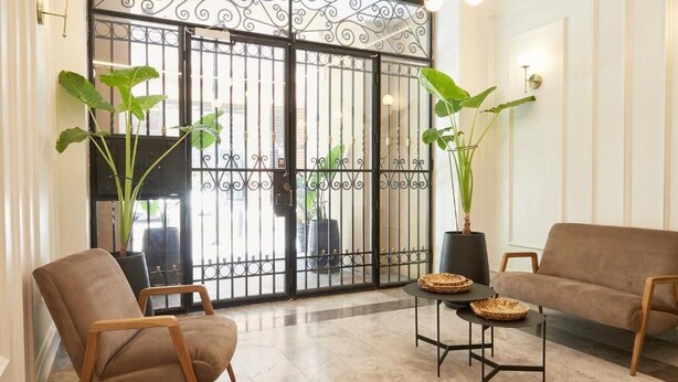 Un interior moderno con un gran portón negro, dos plantas en macetas, un sofá marrón y una pequeña mesa con cestas tejidas.