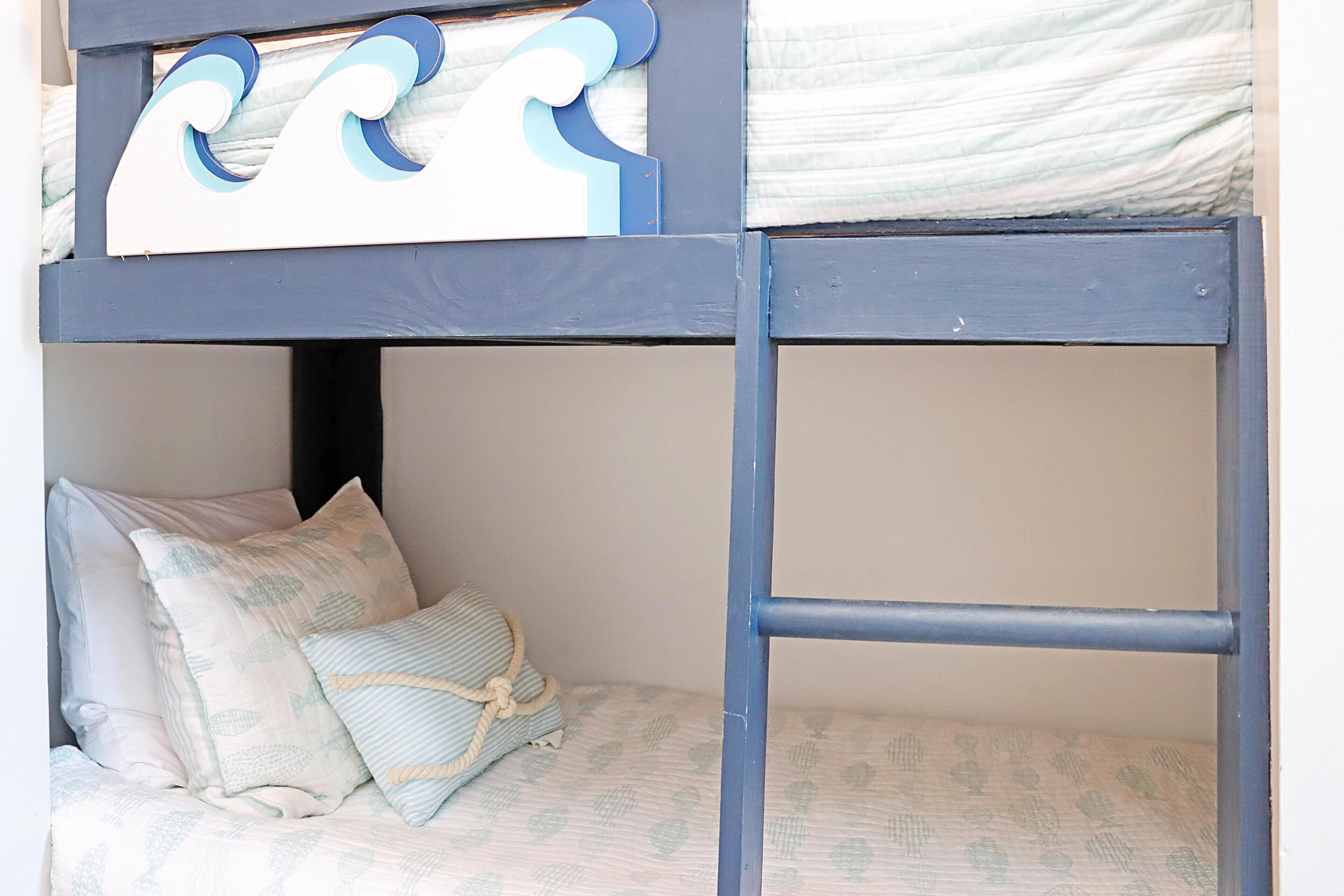 Ein Etagenbett mit Wellenmuster am Kopfteil, ein Kissen mit Blättermotiv und eine Kordel um das Kissen.