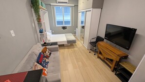 Ein kleiner Wohnbereich mit einer Couch, einem Bett, einem Fernseher und einem Holztisch.