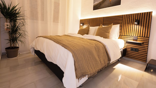 A modern bedroom with a large bed, a wooden headboard, a nightstand with a lamp, and a potted plant. - Comfy Stylish Stay in Malaga (Malaga)