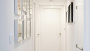 A clean, white hallway with a tiled floor, a door at the end, and framed pictures on the walls. - Comfy Stylish Stay in Malaga (Malaga)