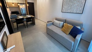 Een moderne woonkamer met een grijze bank, een eethoek met een tafel en stoelen, en een keuken op de achtergrond.