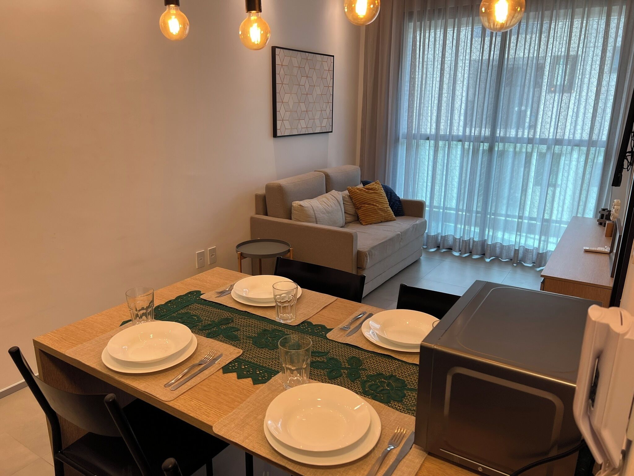 Een eethoek met een tafel voor vier personen, een bank en een raam met dunne gordijnen.