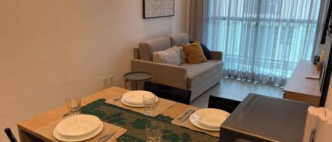 Een eethoek met een tafel voor vier personen, een bank en een raam met dunne gordijnen.