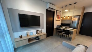 Een moderne woonkamer met een flatscreen televisie, een bank en een eethoek met een tafel en stoelen.