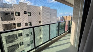 Een balkon met een hek van gaas, een betegelde vloer en uitzicht op omliggende gebouwen.