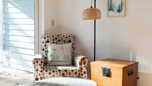A room with a polka-dotted armchair, a round ottoman, a wooden side table, a floor lamp, and a framed picture on the wall. - Relaxing River Lodge • Hot Tub • Family Friendly (Rhododendron)